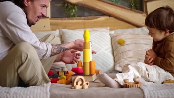 Père jouant avec son fils avec des jouets en bois colorés et écologiques sur le lit - Séquence, vidéo