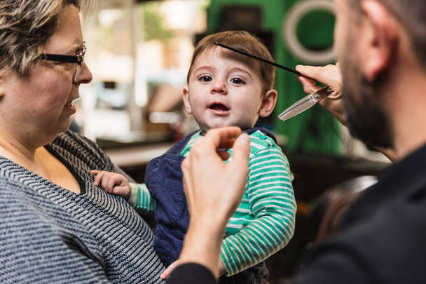 Szívmelengető családi pillanat: kisgyermekek első hajvágás tapasztalat egy professzionális fodrászat egy gondoskodó szülő, szelíd fodrász, és biztonságos biztonsági olló - Fotó, kép