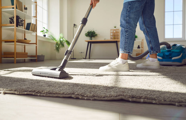Cropped photo of woman cleaning with vacuum cleaner carpet in the living room at home. Female janitor vacuuming the floor. Cleaning service, housekeeping, housework and household concept. - Fotoğraf, Görsel