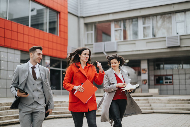 Three professional business associates confidently walking and conversing by a contemporary office, engaging in a discussion with documents in hand. - Photo, Image