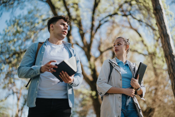 Kültéri kép két fiatal diákról, akik könyveket tartanak, és egy egyetemi parkban beszélgetnek az órákról. - Fotó, kép