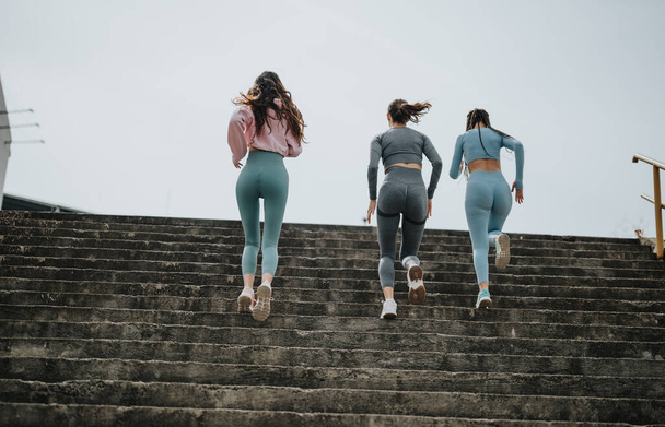 Три жінки в спортивному одязі бігають по сходах, демонструючи активний спосіб життя і командну роботу у фітнесі. - Фото, зображення