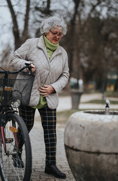 Volwassen vrouwelijke gepensioneerde staan met haar fiets buiten, presentatie van een actieve levensstijl en vrije tijd in pensionering. - Foto, afbeelding