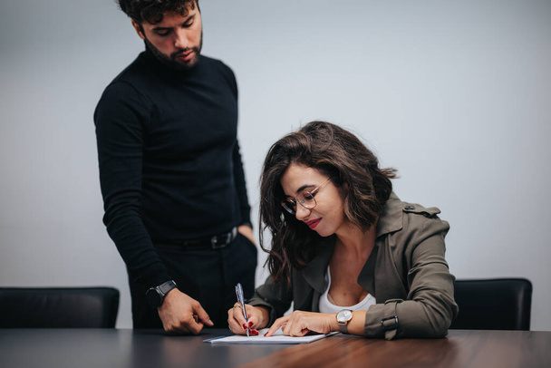 Modern bir ofis ortamında dikkatli bir erkek meslektaşla evrakları imzalayan odaklanmış bir iş kadını. Profesyonel takım çalışmasının ve anlaşmanın açıklanması. - Fotoğraf, Görsel