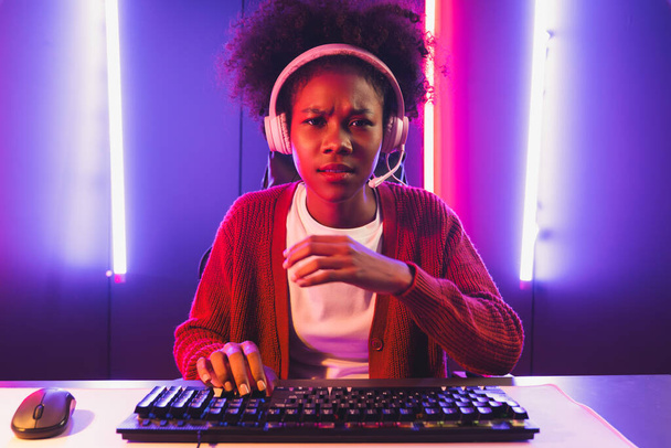 Gaming streamer, ragazza africana che gioca online combattendo con Esport squadra abile indossando cuffie nella stanza di illuminazione al neon colore. Parlare di altri giocatori che pianificano strategie per vincere i concorrenti. Tastificatore. - Foto, immagini