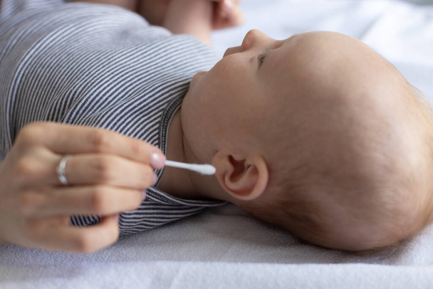 Vrouwelijke hand met verkeerde wattenstaafje in het oor van een baby. Gevaarlijke oren reinigen van de baby 's. Sluitingsdatum. - Foto, afbeelding