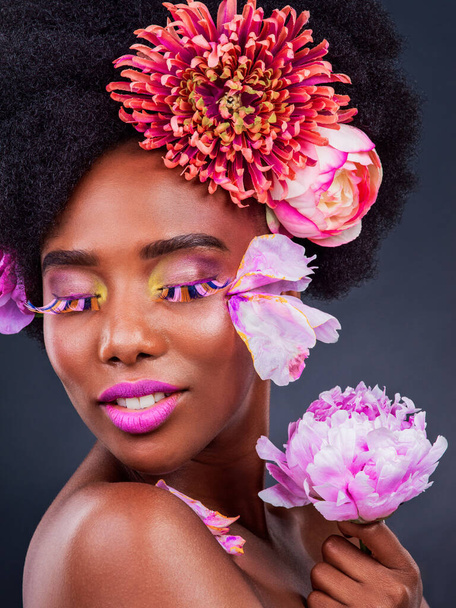 African, woman and beauty with flowers, smile and lashes for makeup, skincare and confidence in studio. Female person, pose and happy for fashion, style and luxury in grey background for cosmetics. - Photo, Image