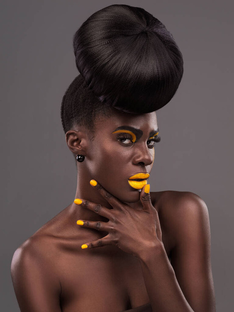 African, woman and studio color with makeup, beauty and creative yellow lipstick. Bold, model and skin with confidence, dramatic hair and bun for glamour or trendy cosmetics on grey studio background. - Photo, Image