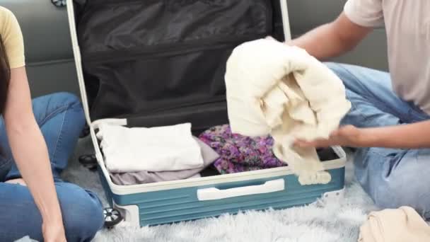 Un couple asiatique emballe ses vêtements pour un voyage à l'étranger en les fourrant dans des valises sur le sol du salon pendant qu'ils se préparent pour leurs vacances. - Séquence, vidéo