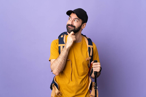Homem bonito caucasiano com mochila e postes de trekking sobre fundo isolado pensando uma ideia enquanto olha para cima - Foto, Imagem