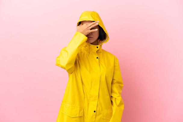 Junge lateinamerikanische Frau trägt einen regendichten Mantel über isoliertem Hintergrund mit Kopfschmerzen - Foto, Bild