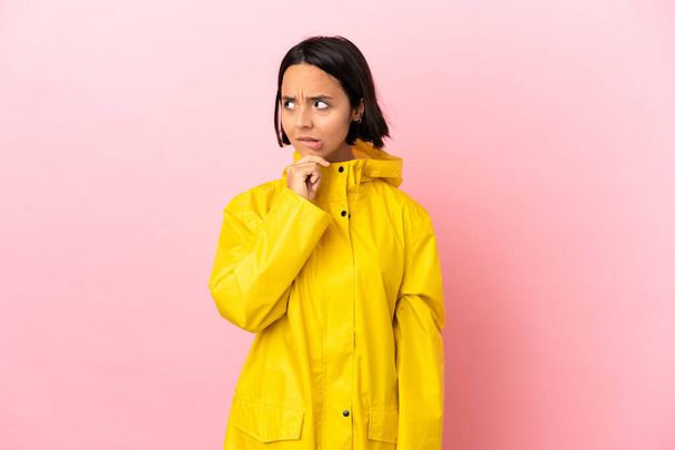 Junge lateinamerikanische Frau trägt einen regendichten Mantel über isoliertem Hintergrund, hat Zweifel und denkt nach - Foto, Bild