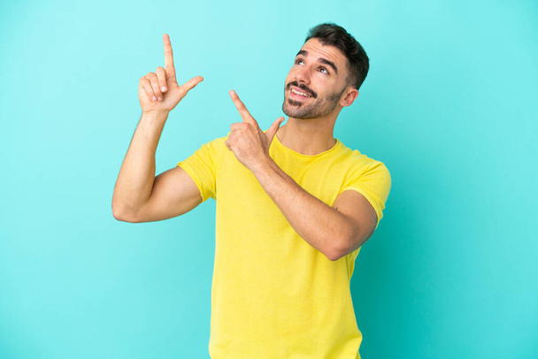 Junger kaukasischer Mann isoliert auf blauem Hintergrund und zeigt mit dem Zeigefinger auf eine großartige Idee - Foto, Bild