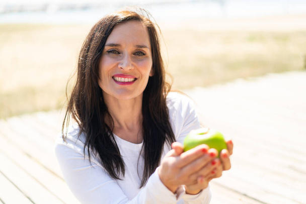 Μεσήλικη γυναίκα που κρατάει ένα μήλο με χαρούμενη έκφραση - Φωτογραφία, εικόνα