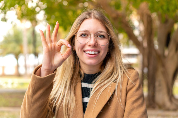 Junge hübsche blonde Frau im Freien zeigt ok Zeichen mit Fingern - Foto, Bild