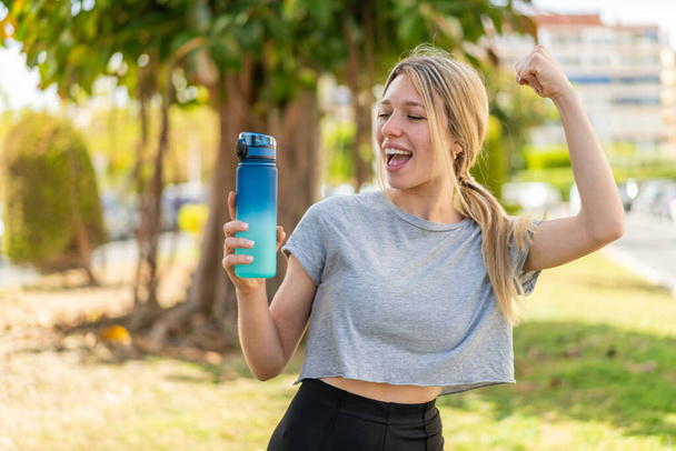 Mladá blondýnka sportovní žena s lahví vody venku slaví vítězství - Fotografie, Obrázek