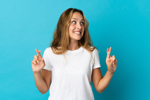 Young blonde woman isolated on blue background with fingers crossing - Photo, Image