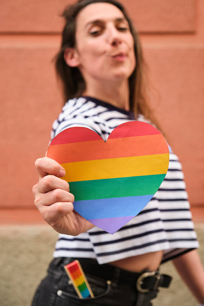 Femme lesbienne trans tenant fièrement un cœur arc-en-ciel dans sa main pendant le Mois international de la fierté. - Photo, image
