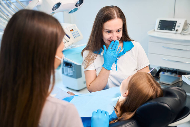 Une hygiéniste et une assistante prennent rendez-vous dans un cabinet dentaire, une patiente est assise sur une chaise - Photo, image
