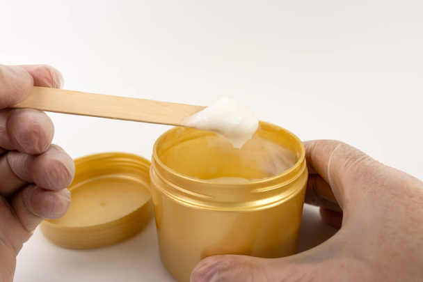 A cosmetic gel from a plastic jar is applied to a wooden spatula. - Photo, Image