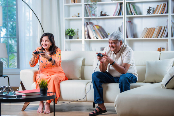 インドのシニアカップルは,自宅でソファーに座っている間,楽しいビデオゲームをプレイしています - 写真・画像