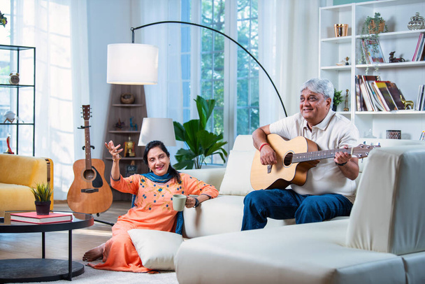 Starsza indyjska para śpiewa razem piosenkę podczas gry na gitarze w domu, ciesząc się czasem wolnym - Zdjęcie, obraz