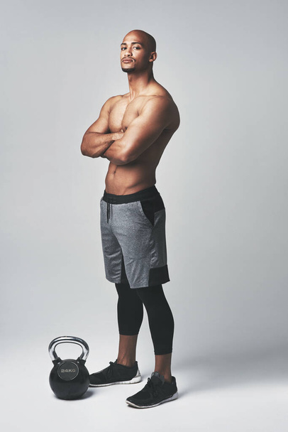 Μαύρος άνδρας, πορτραίτο και κέτλμπελ στο στούντιο, αυτοπεποίθηση και shirtless για προπόνηση ή άσκηση. Άνδρας, αθλητής και άρση βαρών για την πρόοδο των μυών σε γκρι φόντο, σκληρή και πρόκληση. - Φωτογραφία, εικόνα