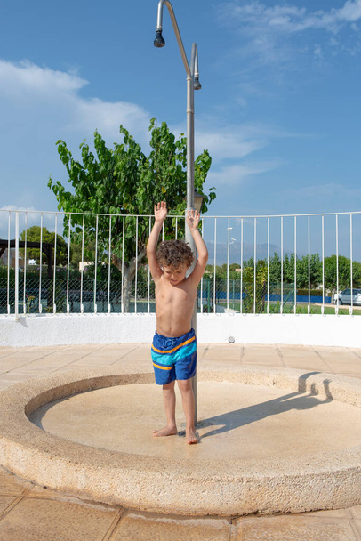 Bambino che si gode una doccia a bordo piscina in una giornata di sole. - Foto, immagini