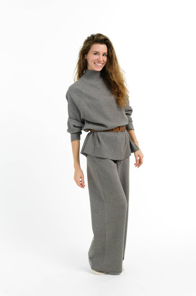 Eine Frau mit strahlendem Lächeln, die einen schicken grauen Pullover und eine weite Beinhose trägt. Ihre Haare fallen in den Nacken, die Ärmel hochgekrempelt, strahlen Vertrauen in ihre Mode-Design-Kleidung aus. - Foto, Bild