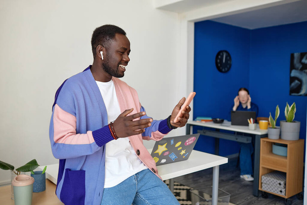 Живой портрет современного черного мужчины, использующего смартфон с видеочатом в креативном офисном пространстве - Фото, изображение