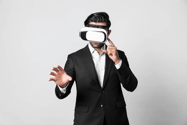 VRメガネを着用しながら何かを持っているプロのスマートなビジネスマン. 仮想現実ゴーグルを搭載したコーカサスプロジェクトマネージャーは,ホワイトバックグラウンドで技術革新を提示します. デバイス. - 写真・画像
