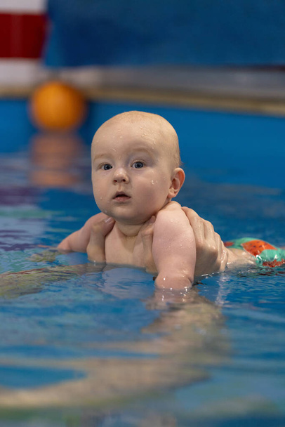 スイミングプールで好奇心旺盛な赤ちゃんの肖像画。 コーチと一緒に泳ぐ - 写真・画像