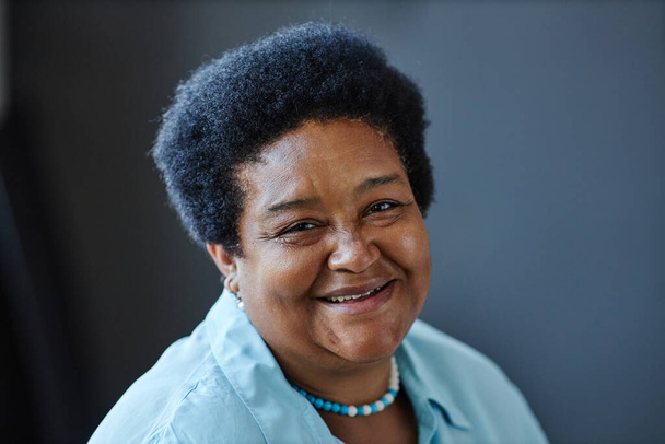Счастливая взрослая афроамериканка-пенсионерка в голубой рубашке смотрит в камеру с улыбкой на сером фоне в изоляции - Фото, изображение