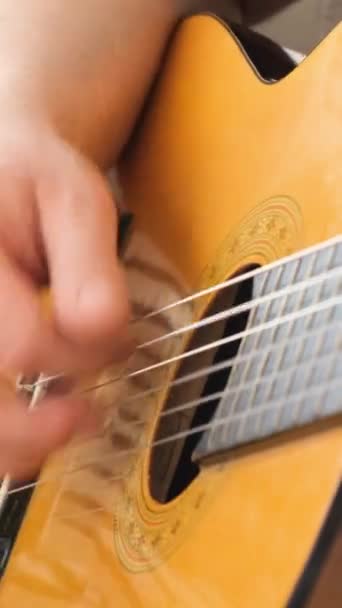 Közelkép valakiről, aki egy akusztikus gitárként ismert hangszeren játszik, egy húros hangszeren. Az emberek ujjaznak vagy rángatják a húrokat, hogy zenéljenek. - Felvétel, videó