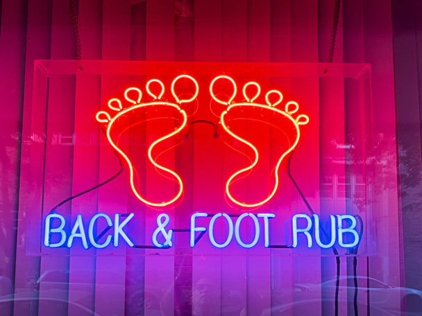 A bright red and blue neon sign illuminates the window of an anonymous massage parlor selling back rubs and foot rubs. - Photo, Image