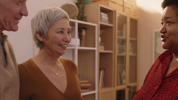 Medium shot van drie vrolijke multiraciale senior vrienden bij elkaar voor het diner in gezellige studio appartement - Video