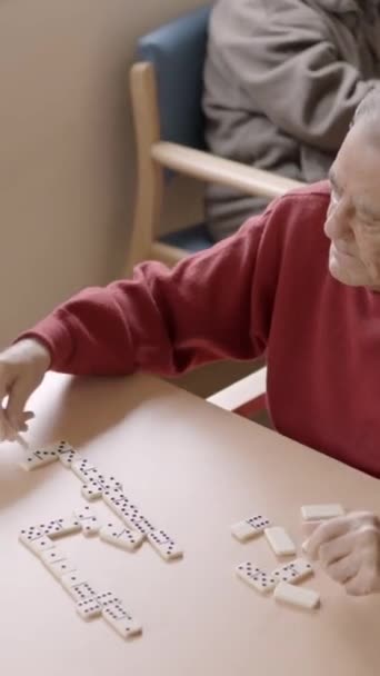 Zpomalené video staršího muže hrajícího domino se starým přítelem v geriatrickém - Záběry, video
