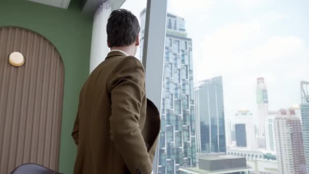 Achteraanzicht ambitieuze zakenman staan in versierd kantoor staren uit raam naar de skyline van de stad. Vastberadenheid en zakelijke ambitie zetten de carrière van het bedrijfsleven in de richting van een goede toekomst - Video
