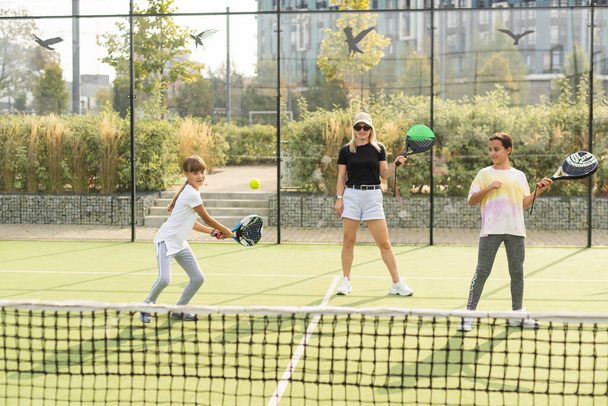 テニスコートに立っている間,子供にテニスを教える陽気なコーチ. 高品質の写真 - 写真・画像