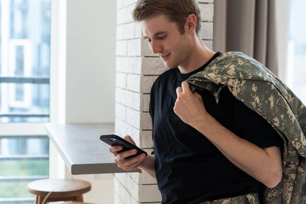 Молодий армійський чоловік використовує смартфон вдома. - Фото, зображення