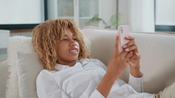 Uma mulher está sentada em um sofá, segurando um celular na mão. Ela aparece focada no dispositivo enquanto interage com ele.. - Filmagem, Vídeo