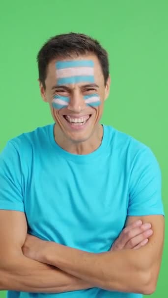 Видео в студии с хромой человека, стоящего с аргентинским флагом, нарисованным на лице, улыбающимся со скрещенными руками - Кадры, видео