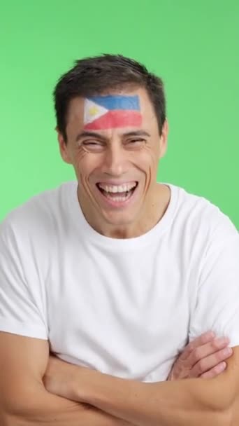 Video in studio met chroma van een man die staat met een Filippijnse vlag geschilderd op gezicht glimlachend met gekruiste armen - Video