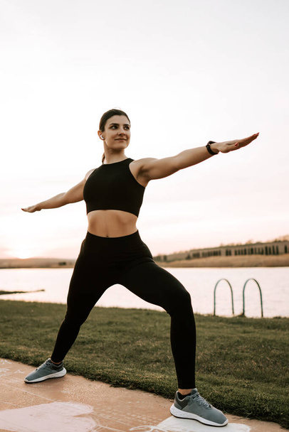 Молодая женщина в спортивной одежде занимается фитнесом на закате на природе. Понятие здорового образа жизни. Фитнес и спорт - Фото, изображение