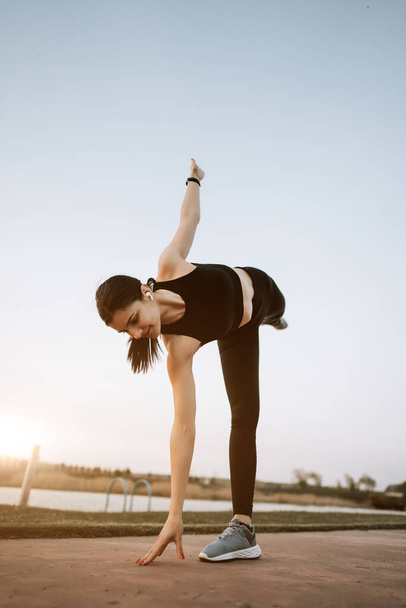 Egy fiatal nő a sportruházatban fitnesz gyakorlatokat végez naplementekor. Egészséges életmód koncepció. Fitness és sport - Fotó, kép