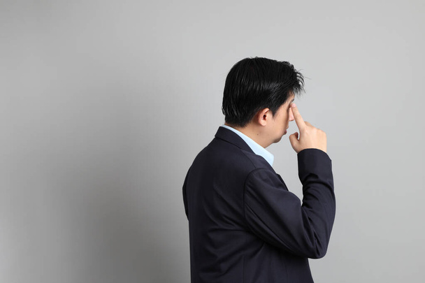 El empresario asiático con formal vestido con gesto de pensar en el fondo gris. - Foto, Imagen