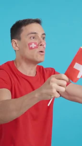 Video en estudio con croma de un hombre mirando hacia otro lado ondeando una bandera nacional suiza, enojado con una decisión de árbitros - Metraje, vídeo