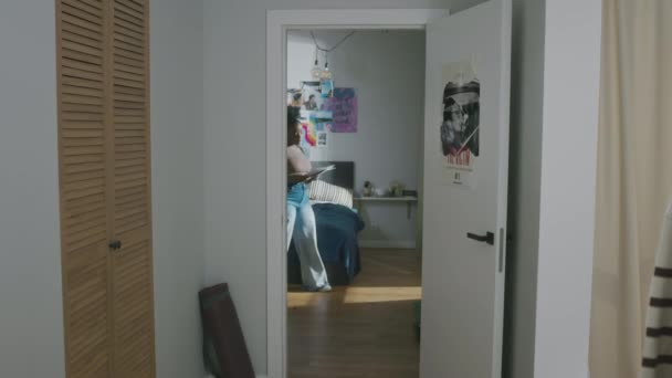 Volledig shot van jonge zwarte vrouwelijke student in ontspannen casualwear wandelen langs appartement met papieren lakens in handen, terwijl leermateriaal voor universitaire examen - Video