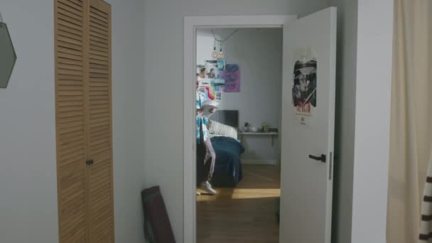 Teljes felvétel kaukázusi diáklányról, aki elhagyja a hálószobáját, és végigmegy a folyosón a modern lakásban, miközben tananyagot tanul a holnapi egyetemi vizsgára. - Felvétel, videó