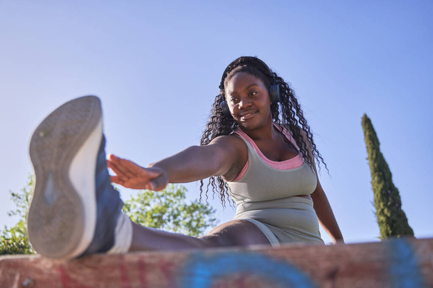 Curvy Afrikalı Amerikalı kadın şehir parkında egzersiz yaparken esneme hareketleri yapıyor. - Fotoğraf, Görsel